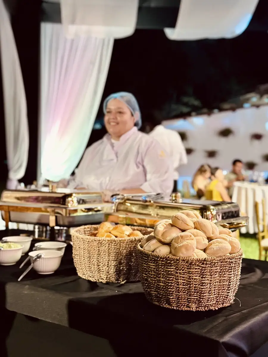 Cocinera con gorro y uniforme blanco sirve pan junto a las fuentes del buffet
