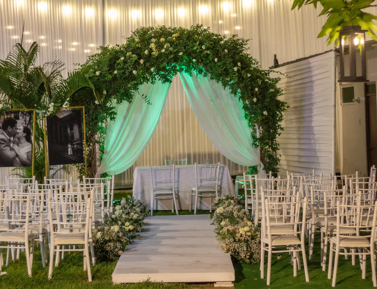 Ceremonia al aire libre con arco floral, pasarela y sillas blancas