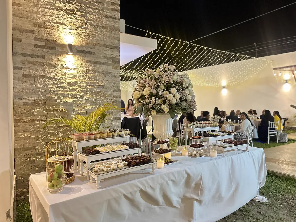 Buffet servido de noche con fuentes, flores blancas y comensales al fondo
