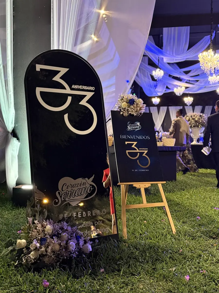 Señalética del aniversario número 33 de una empresa, junto a flores y una entrada iluminada