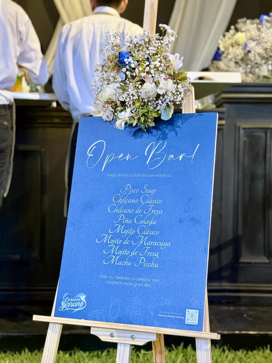 Carta del open bar sobre un atril, con un arreglo floral y la barra detrás