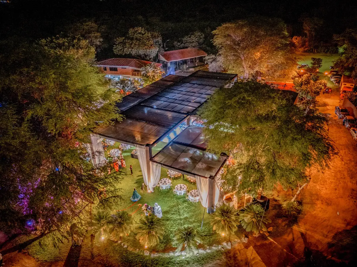 Vista aérea nocturna del toldo iluminado entre jardines y árboles