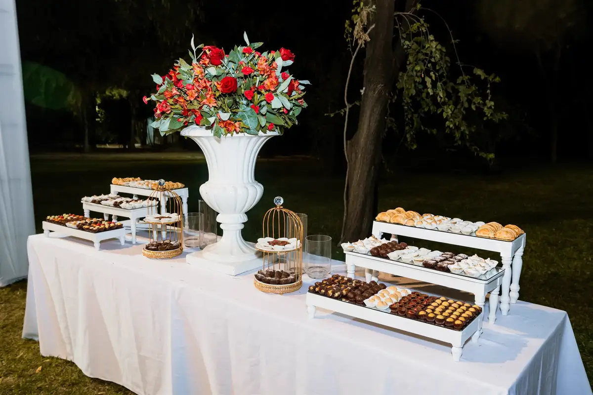 Mesa de dulces con bandejas escalonadas y un arreglo de rosas rojas al aire libre