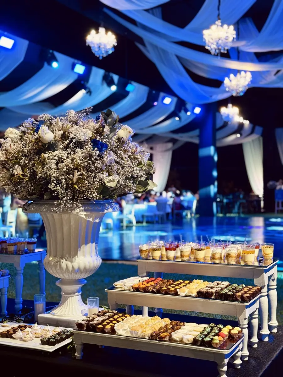 Mesa de bocaditos bajo un toldo con flores y luces azules