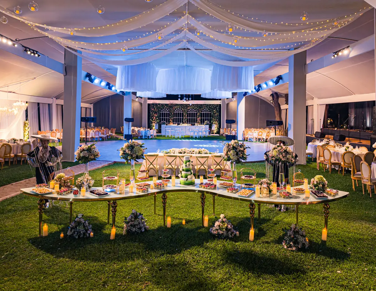 Mesa principal rodeada de jardines, bajo un toldo con luces cálidas