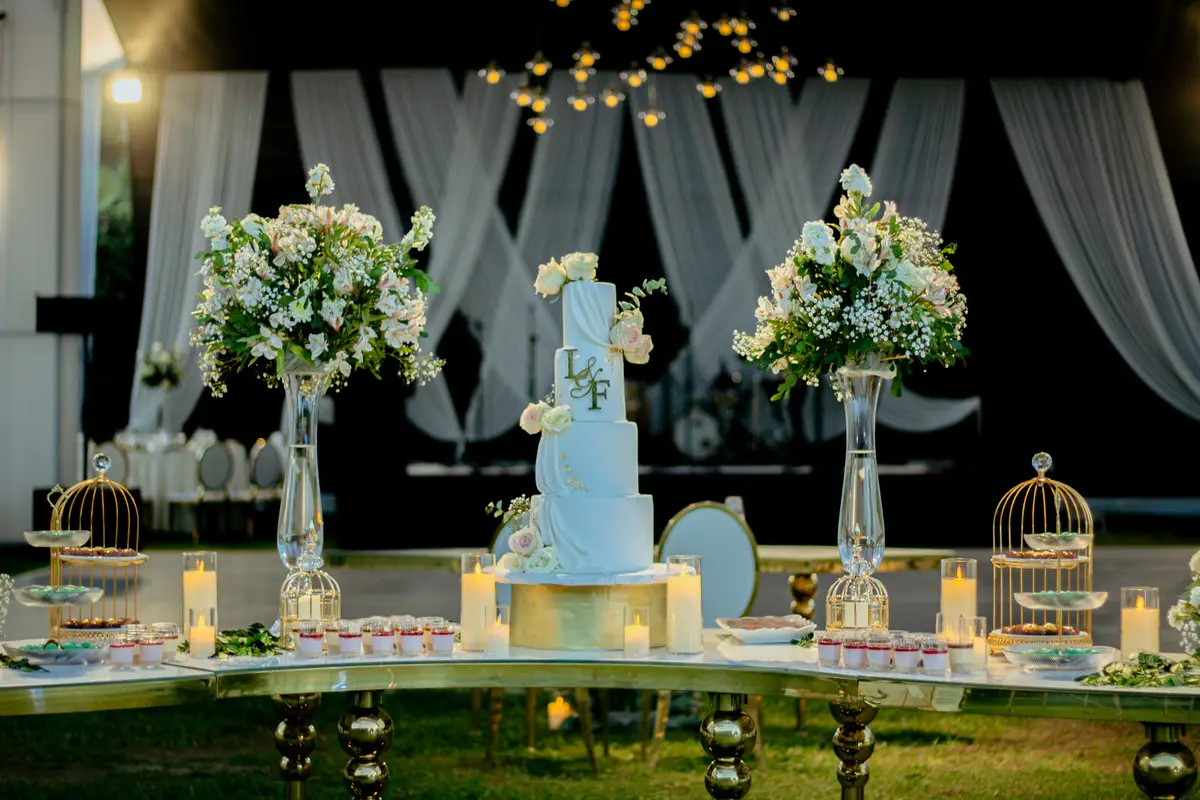 Mesa principal con torta de bodas, flores y luces cálidas bajo el toldo