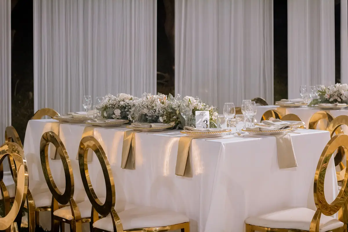Mesas vestidas de blanco y sillas doradas en un salón cálido