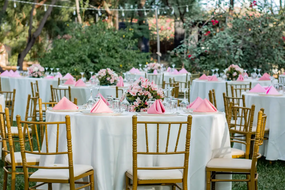 Montaje de mesas redondas con flores rosadas en un jardín frondoso