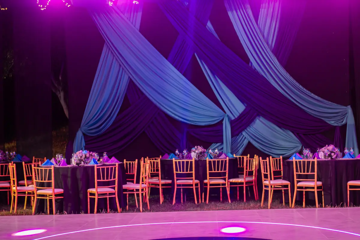 Salón bajo toldo con telas azules y moradas y mesas iluminadas