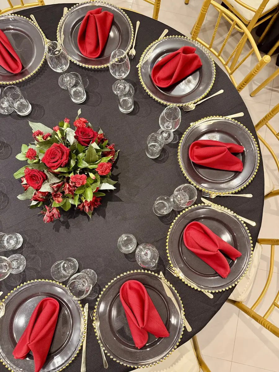 Mesa con mantelería oscura, detalles dorados y flores rojas vista desde arriba