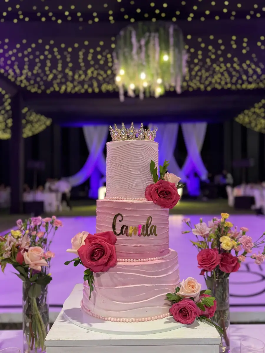 Torta de quinceañera decorada con flores y luces cálidas bajo el toldo