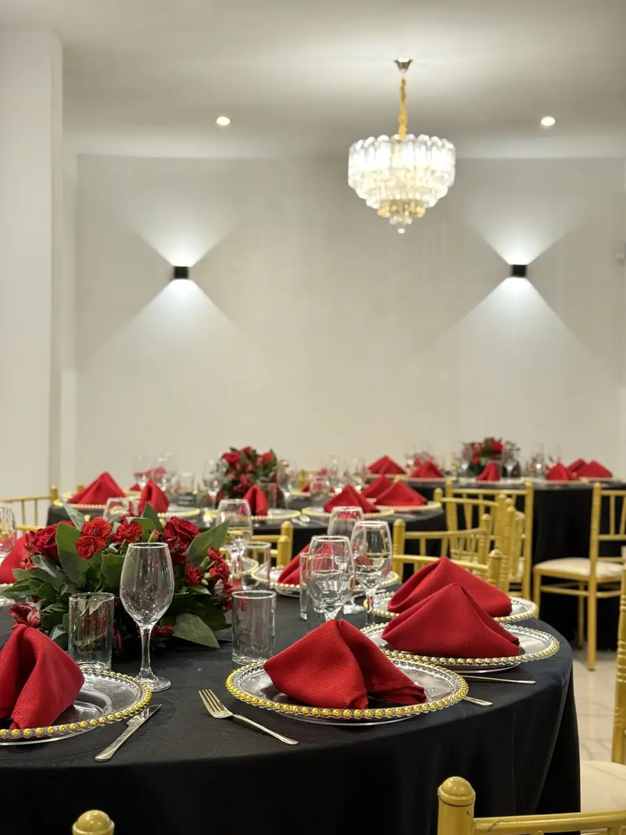 Salón preparado con mesas elegantes, flores rojas y sillas doradas